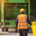 A Waste Management Employee Pulls a Garbage Can towards his truck.