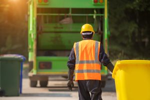 A Waste Management Employee Pulls a Garbage Can towards his truck.