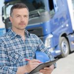 a man holds a clipboard while standing in front of a fleet truck.