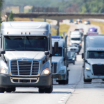 a fleet of 18 wheeler trucks drives down the interstate