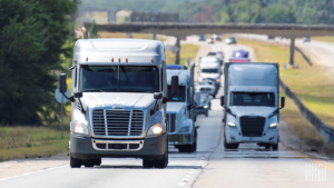 a fleet of 18 wheeler trucks drives down the interstate