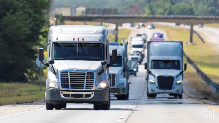 a fleet of 18 wheeler trucks drives down the interstate