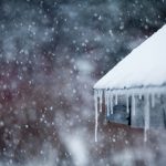 Icicles hang from a room as snow gently falls in the background during Winter.